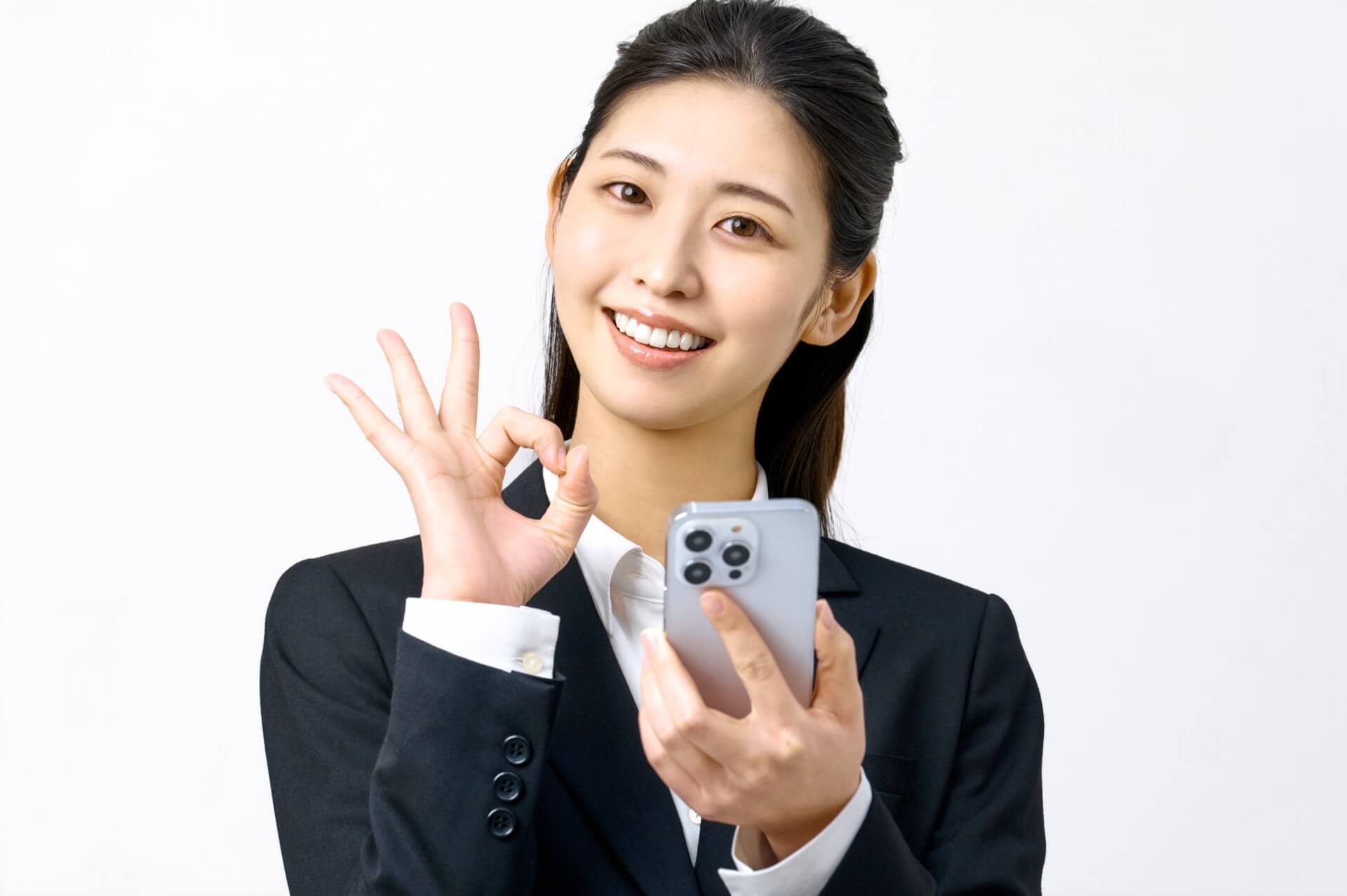 OKサインするスマホを持つ女性の画像。