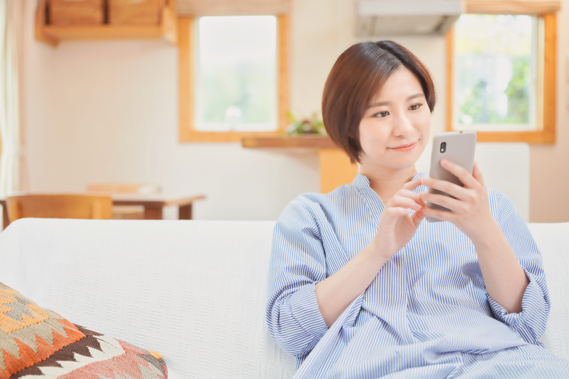 ソファに座りスマートフォンを触っている女性