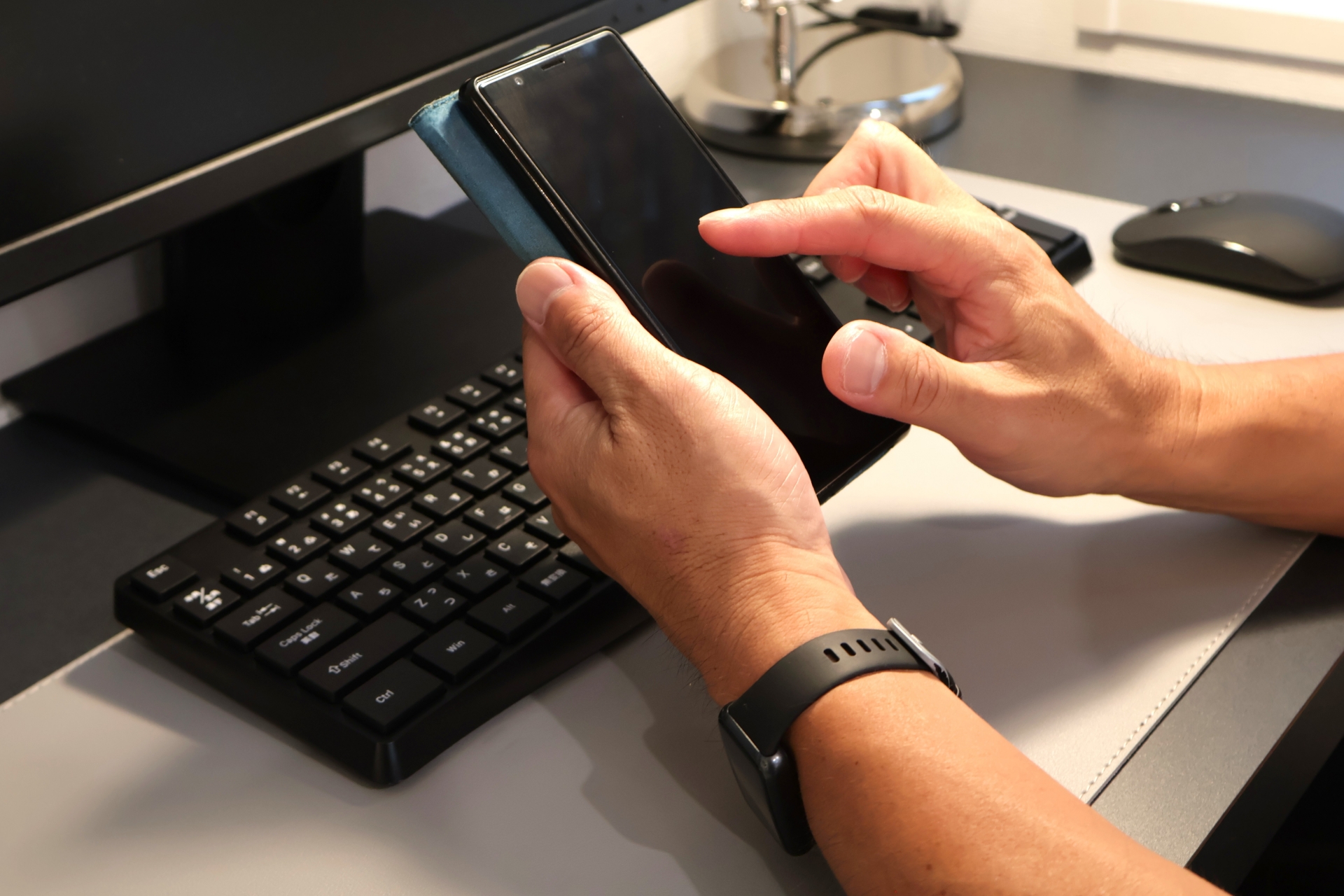 パソコン前でスマホを操作する男性の手元