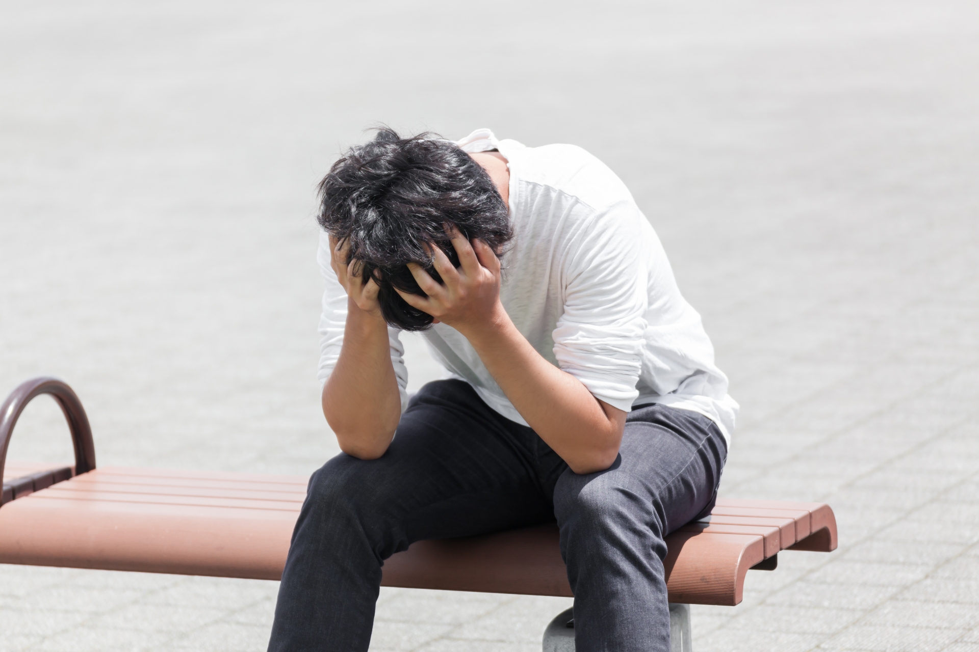 外のベンチで頭を抱えて困っている男性