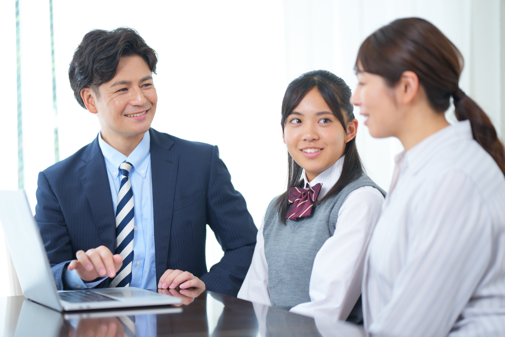 ノートパソコンを見ている女子生徒とお母さんと家庭教師