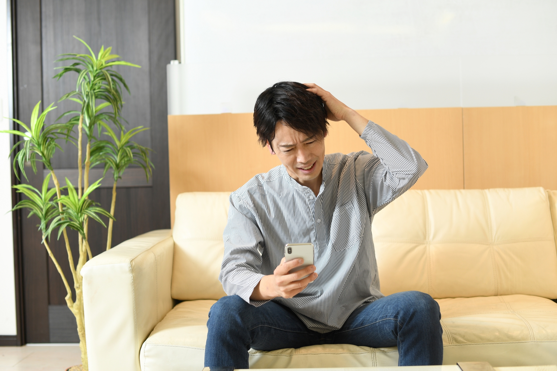頭を抱えながらスマホを見るアジア人男性