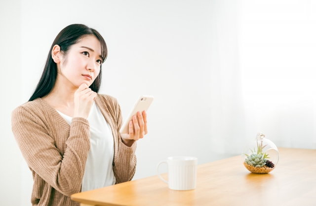 家でスマホのアプリを使いながら考える女性