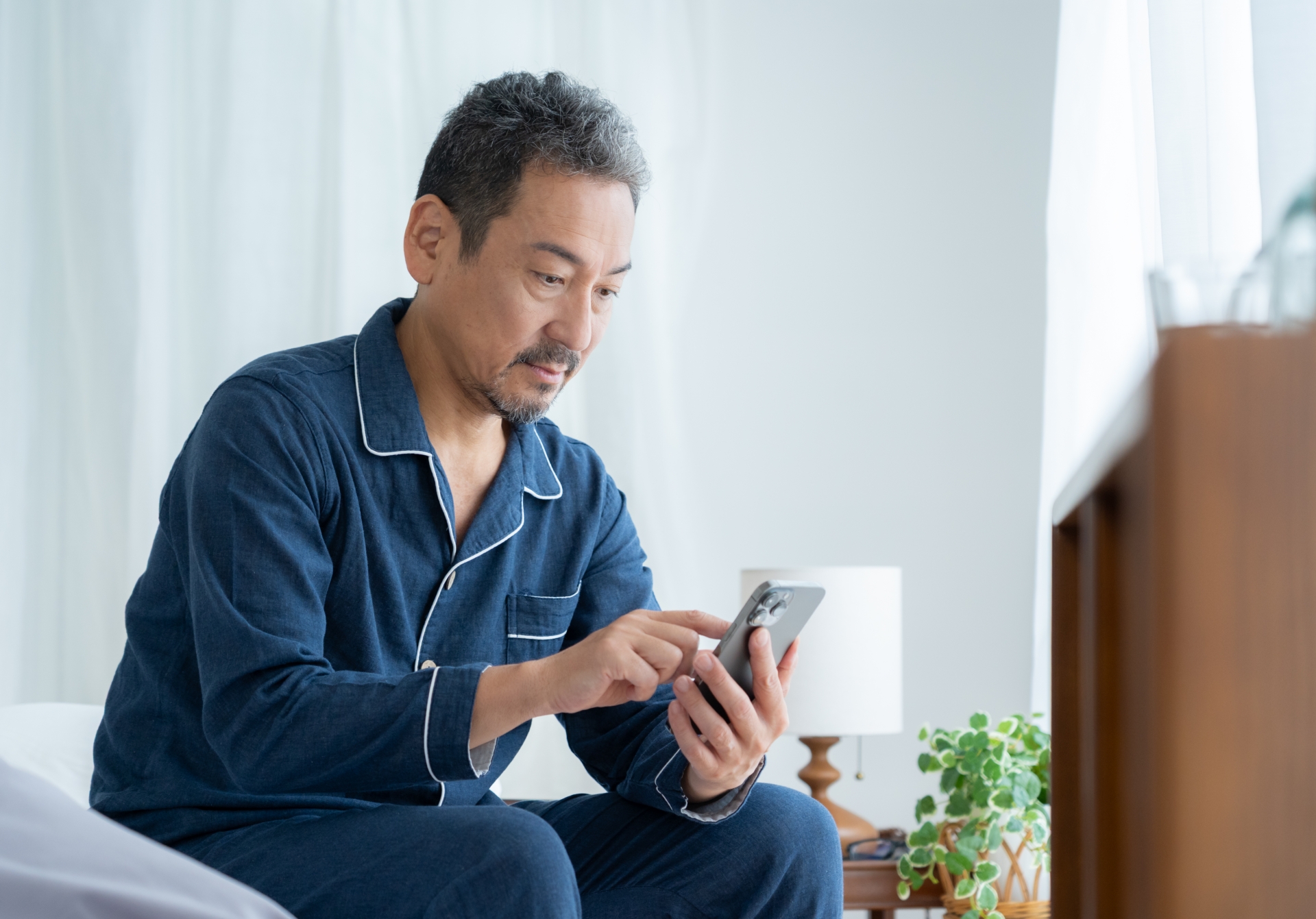 寝室でスマホを見るミドルの男性