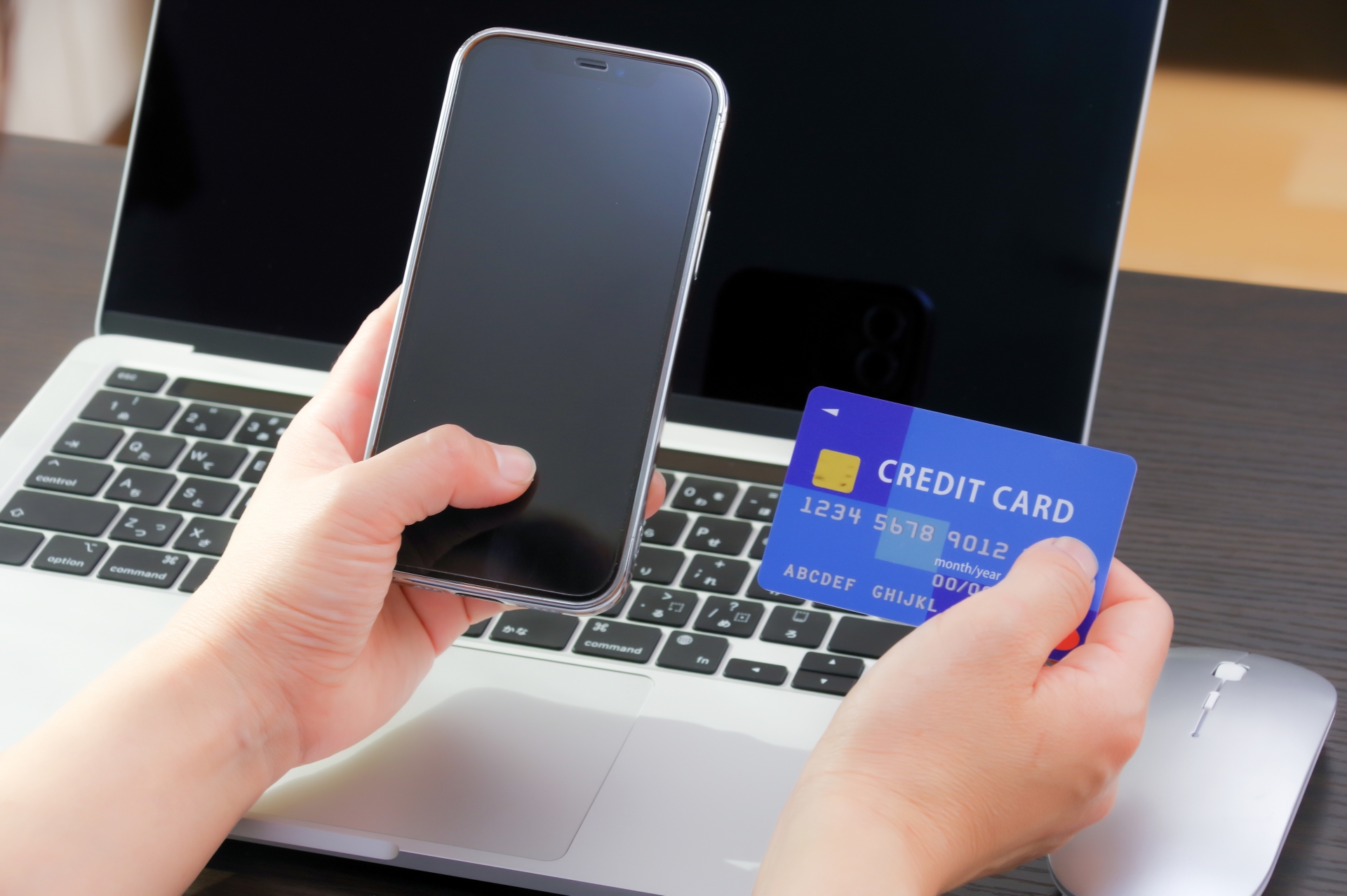 パソコンの前でスマホとクレジットカードを見る人
