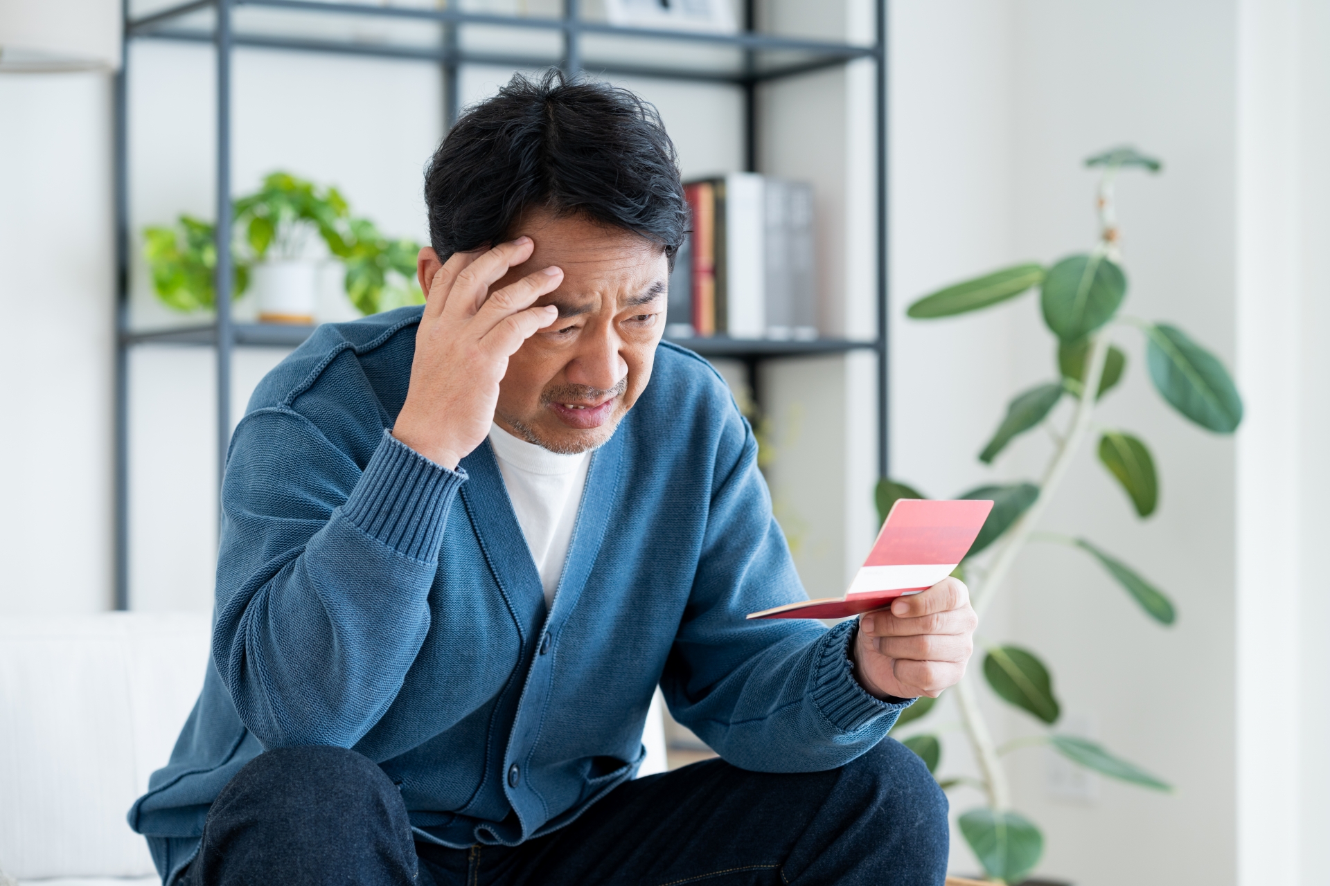 ソファに座って頭に手をやる悩む男性