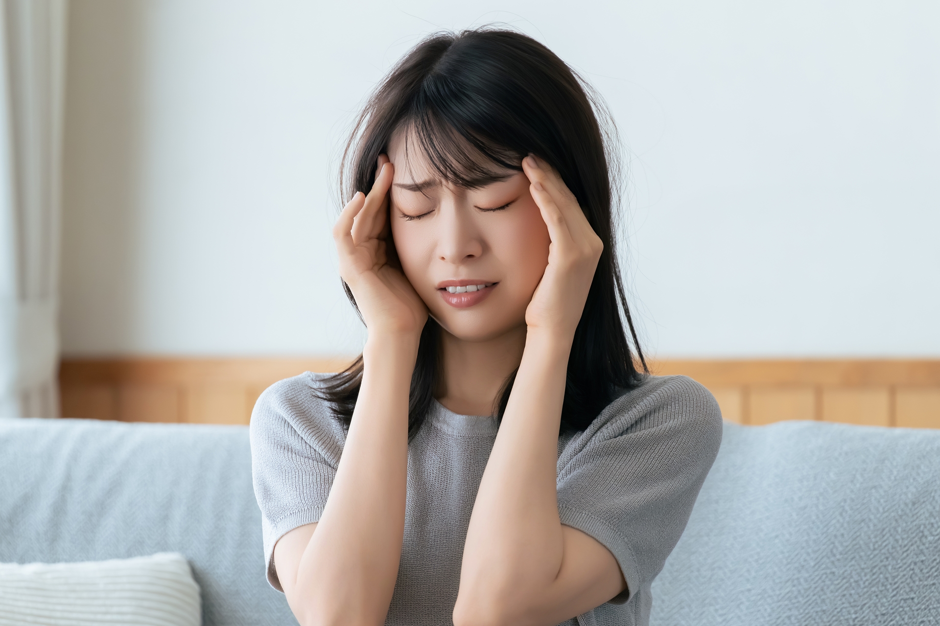 こめかみを手で押さえる辛そうな女性