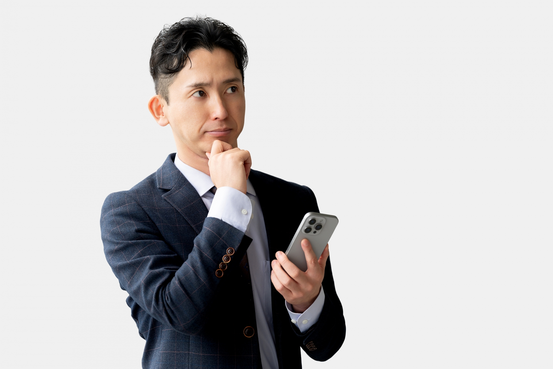あごに手を当てて考えるスマホを持つスーツの男性