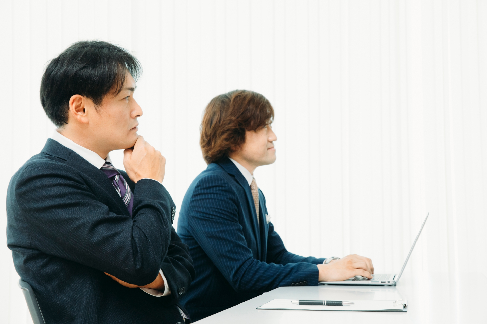 机に座るスーツ姿の男性二人