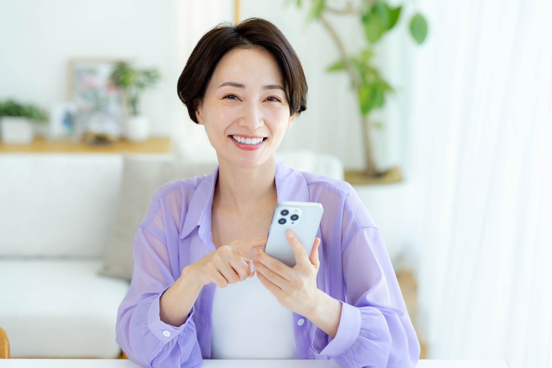 部屋でスマホを操作するミドル女性