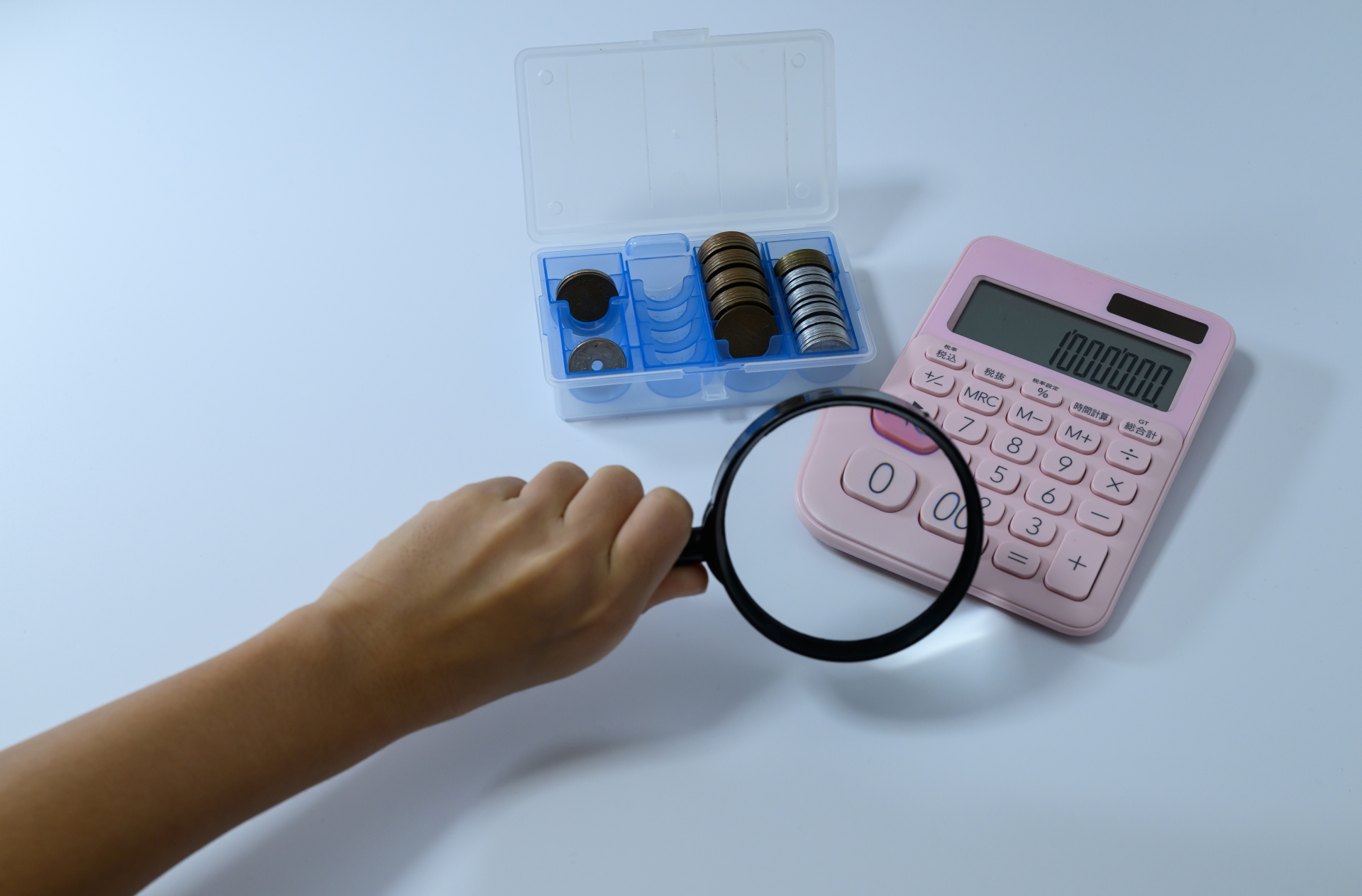 電卓と硬貨を虫眼鏡で覗く手