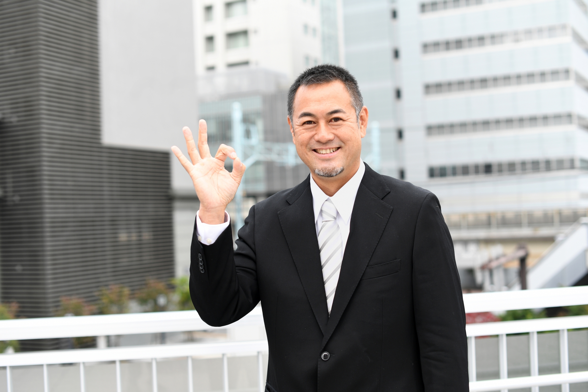 右手を挙げる笑顔のミドルの男性