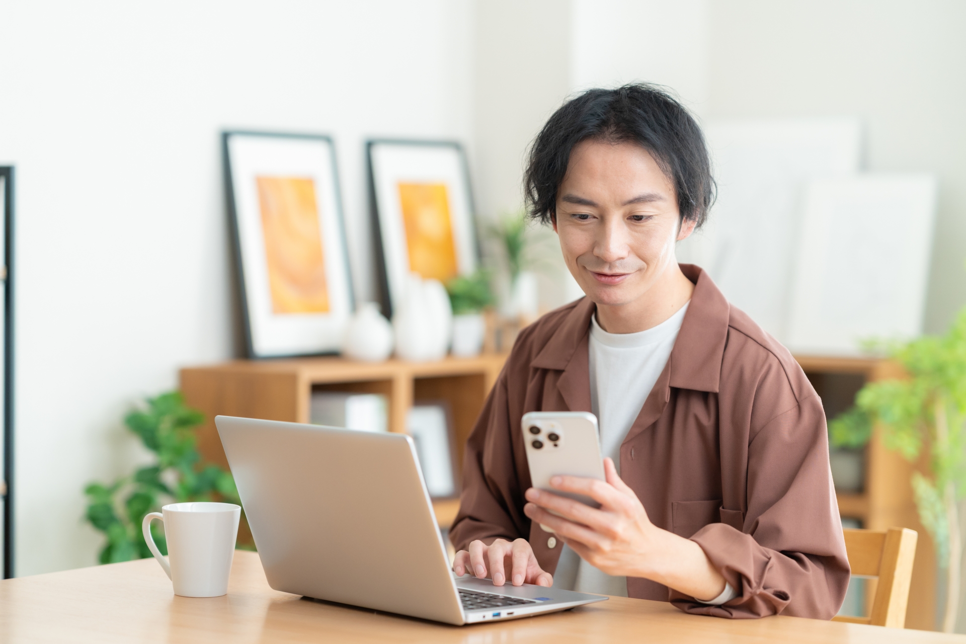 パソコンの前でスマホを見る男性