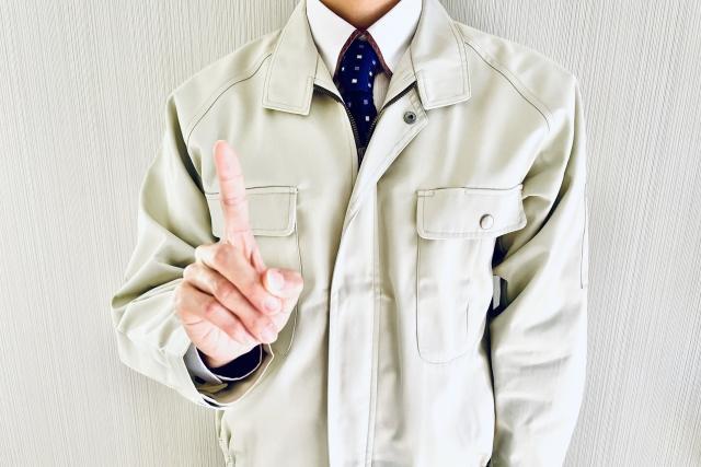 人差し指を立てる作業着姿の男性