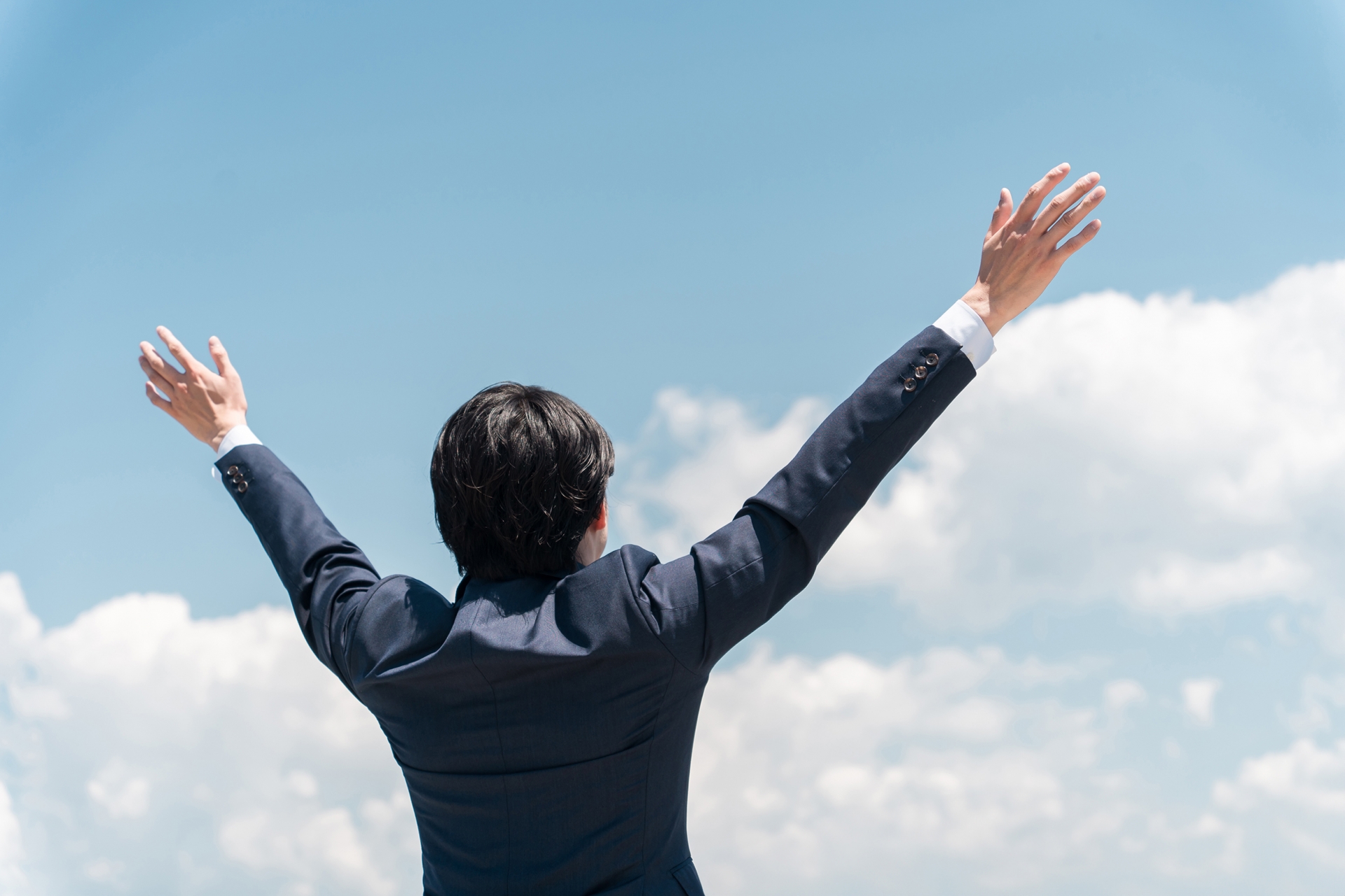 青空に向かって手を広げるビジネスマン