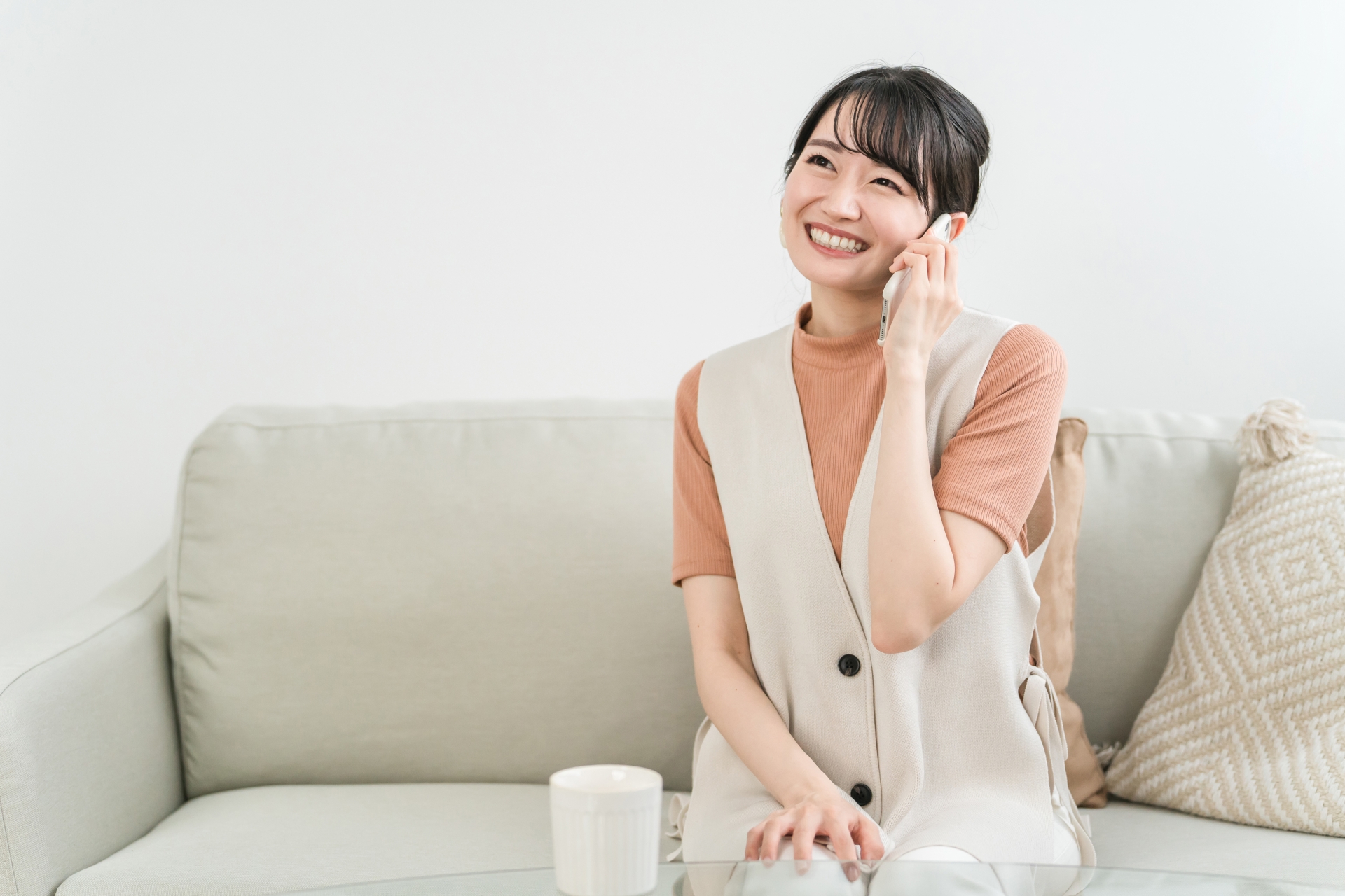 ソファに座ってスマホで電話する笑顔の女性