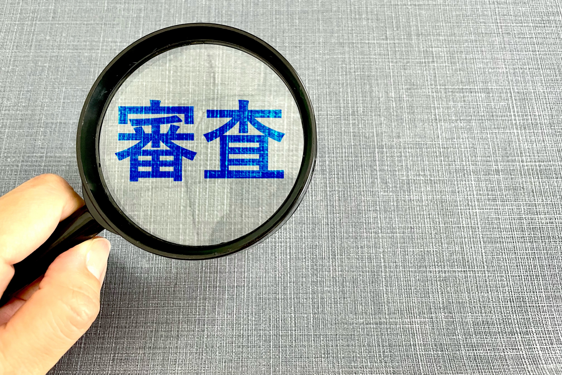 審査の文字と虫眼鏡と手 ビジネスの審査