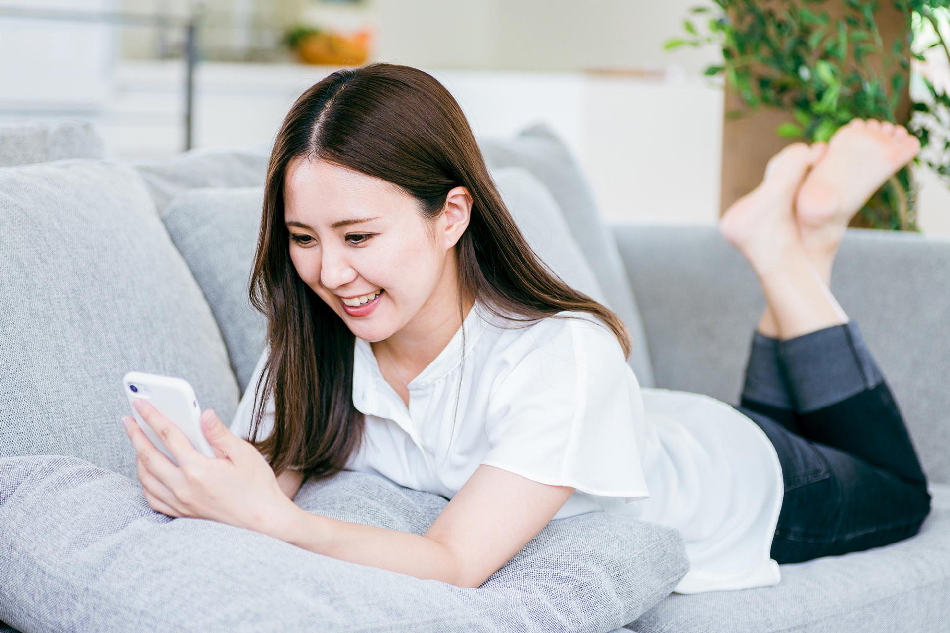 ソファで寝転んでスマホを使う女性