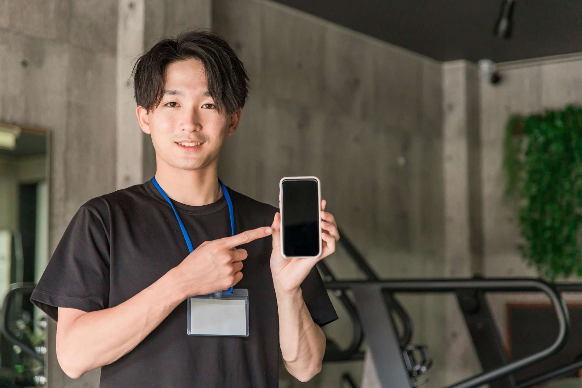 ジムでスマホを持つインストラクターの男性