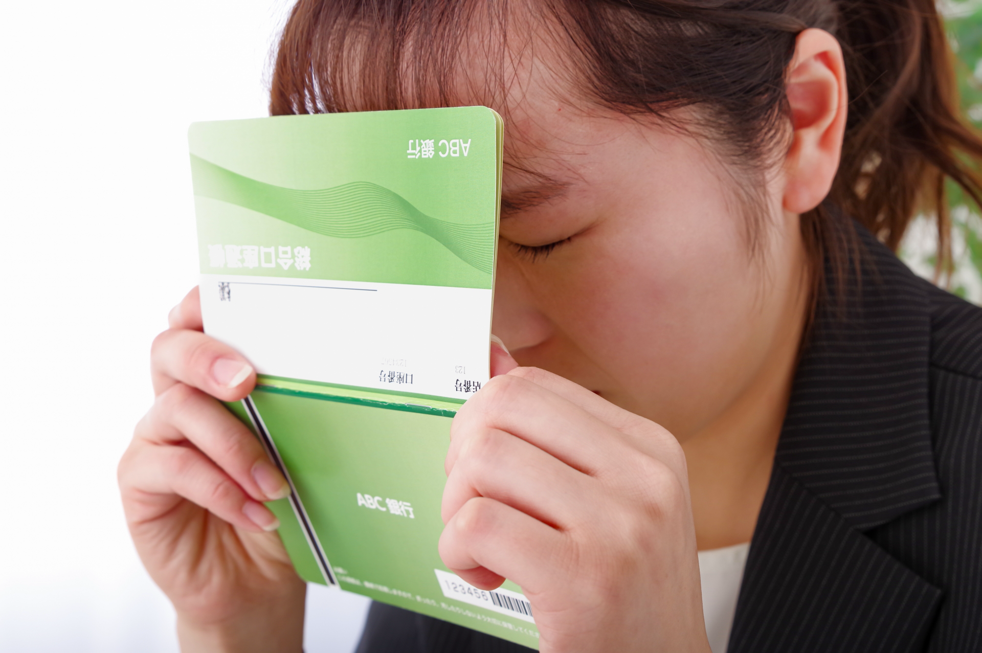 通帳を持ちながら暗い表情をしている女性