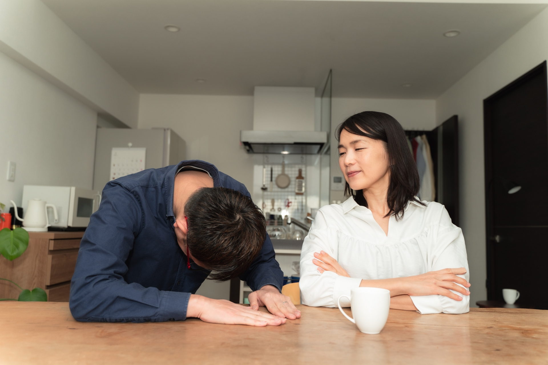 テーブルに手をついて謝る男性と怒る女性