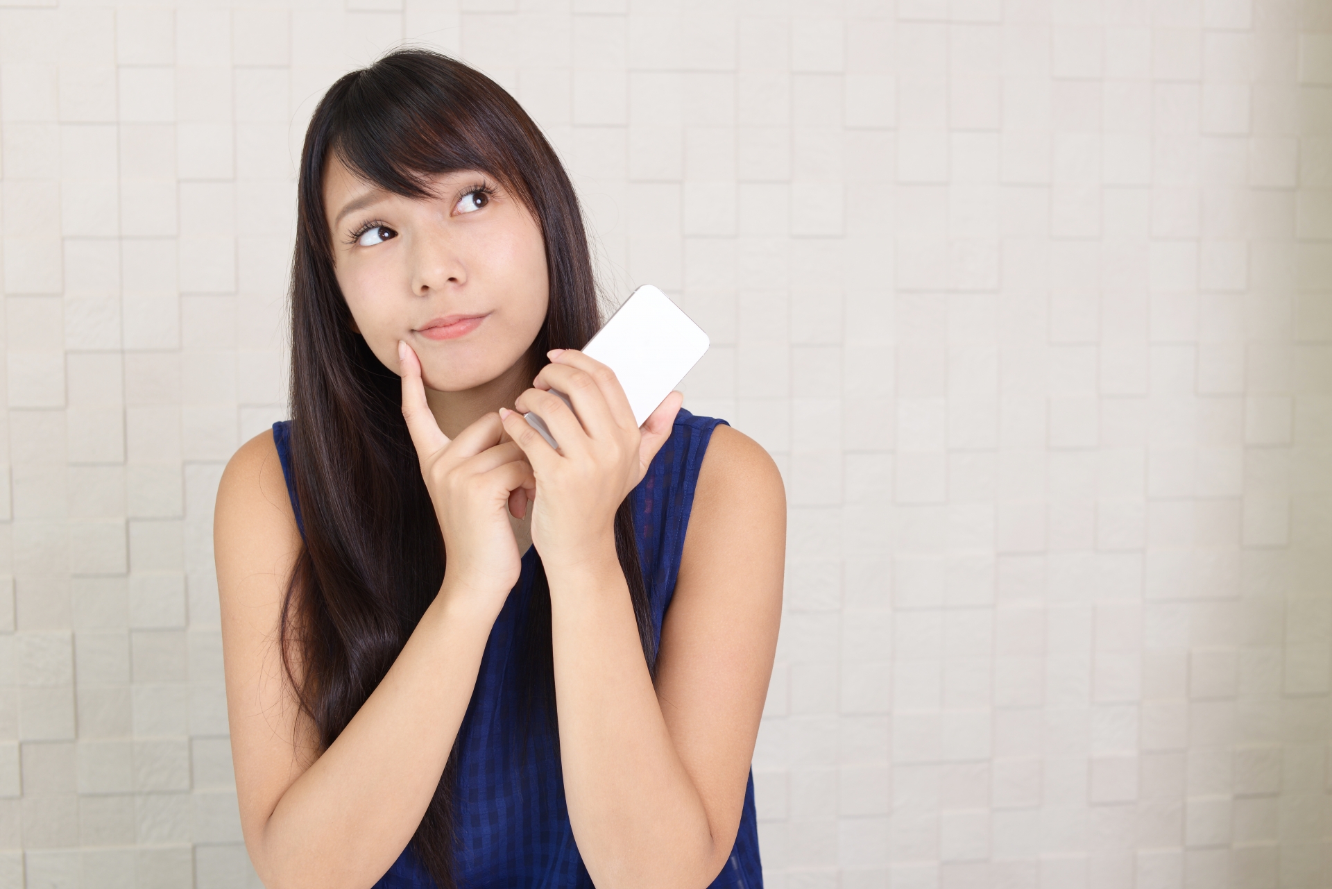 スマートフォンを持って考える女性