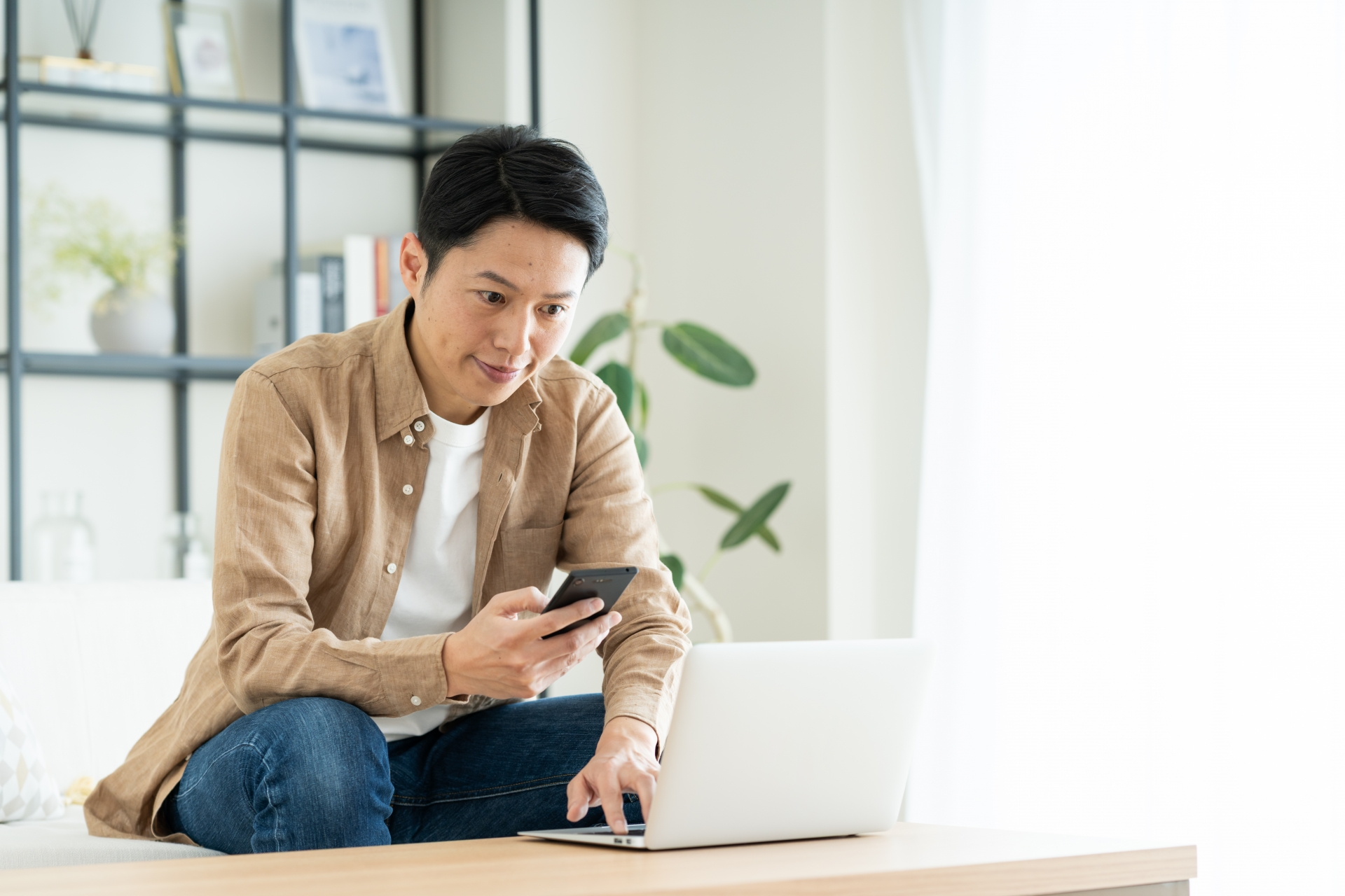 スマホを持ちながらパソコンを操作する男性