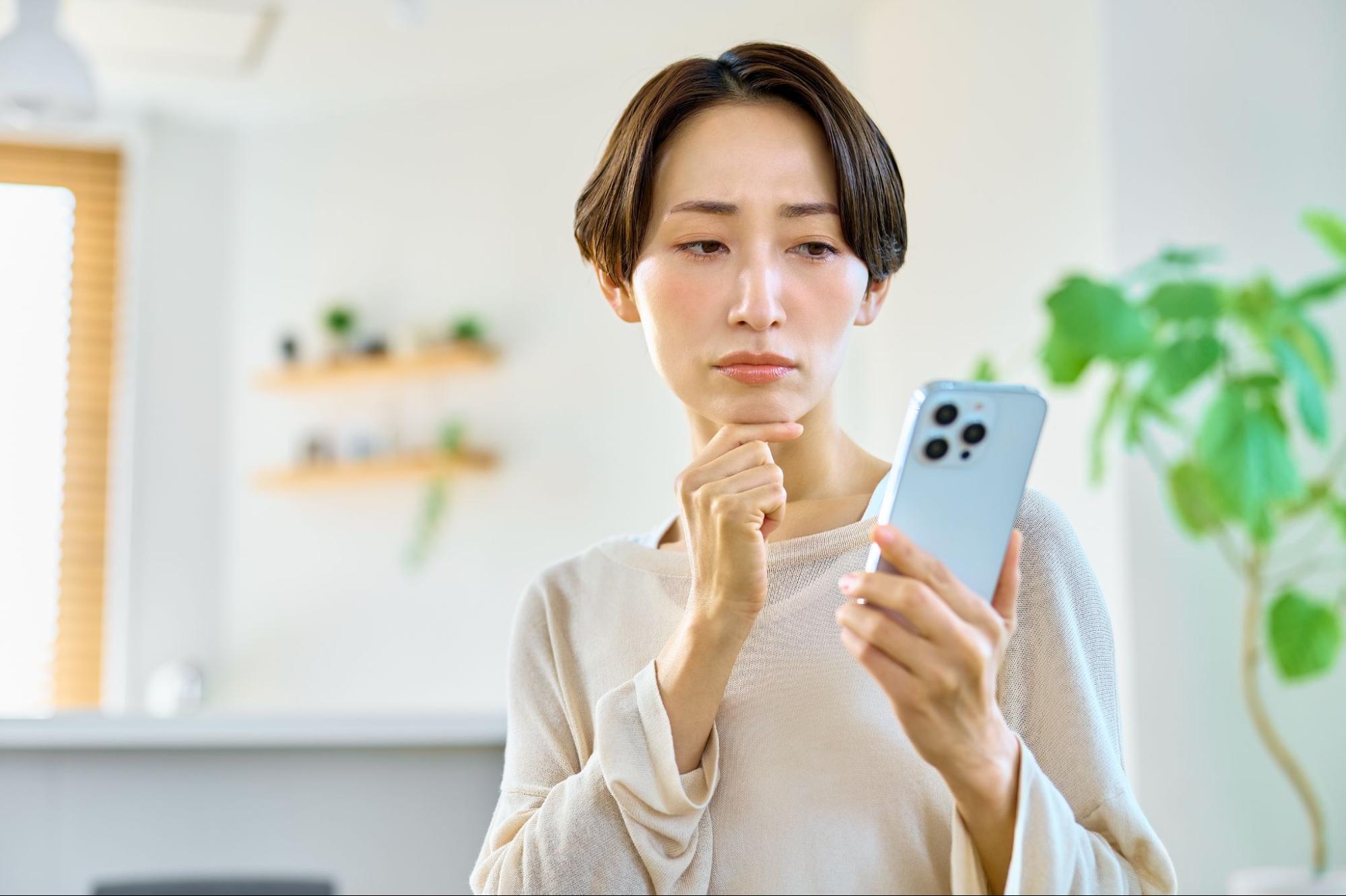 携帯電話を見て悩む女性