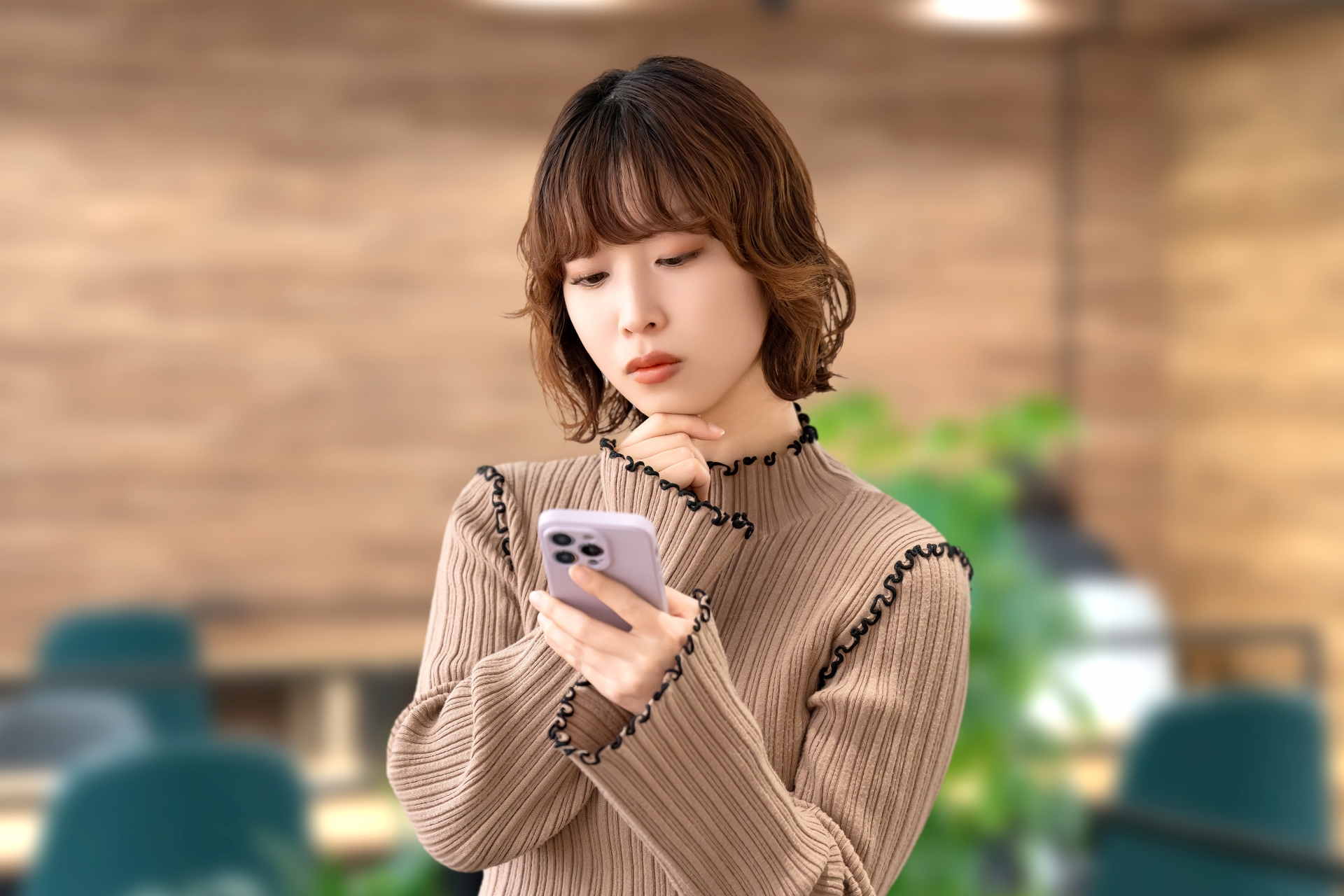 携帯電話を見ながら悩む女性